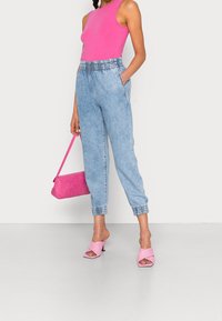 Jasnoniebieskie dżinsowe spodnie dresowe z elastycznym pasem i ściąganymi nogawkami, zestawione z różowym bezrękawnikiem i różową torebką. Różowe klapki na obcasie.