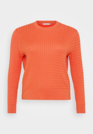 Orange stickad tröja med en texturerad, våffelmönster, rund halsringning och långa ärmar. Litet logotypdetalj på bröstet.