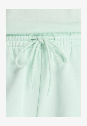 Cintura elastica verde chiaro con coulisse intrecciata annodata su pantaloni o pantaloncini in tessuto morbido.