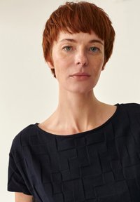 Tumši zila teksturēta augšdaļa ar kvadrātu rakstu. Piedāvā platai kakla izgriezumam un īsām piedurknēm, izgatavota no mīksta materiāla.