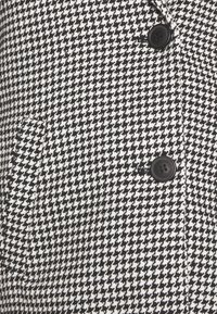 Tela de estampado de espiga en blanco y negro, con dos botones negros y un bolsillo lateral, con un tejido texturizado y un diseño estructurado.