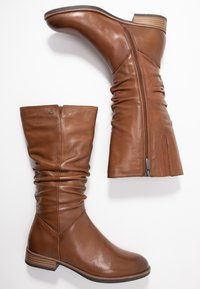 Bottes hautes en cuir marron jusqu'au genou avec un design froissé, fermeture éclair latérale et talon empilé ; texture lisse et style minimaliste.