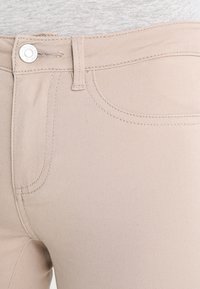 Jeans in denim beige chiaro con una texture liscia, design standard a cinque tasche e chiusura classica con bottone e zip in vita.