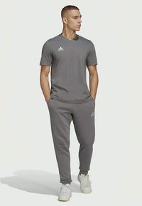 Graues Sport-T-Shirt und passende Jogginghosen aus einem glatten Stoff. Das T-Shirt hat kurze Ärmel; die Jogginghosen verfügen über Seitentaschen und Bündchen.