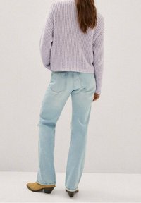 Vaaleansiniset farkut suoralla lahkeella, joissa on kulunut rakenne ja kulutetut yksityiskohdat, yhdistettynä löysään laventelin väriseen neulepuseroon.