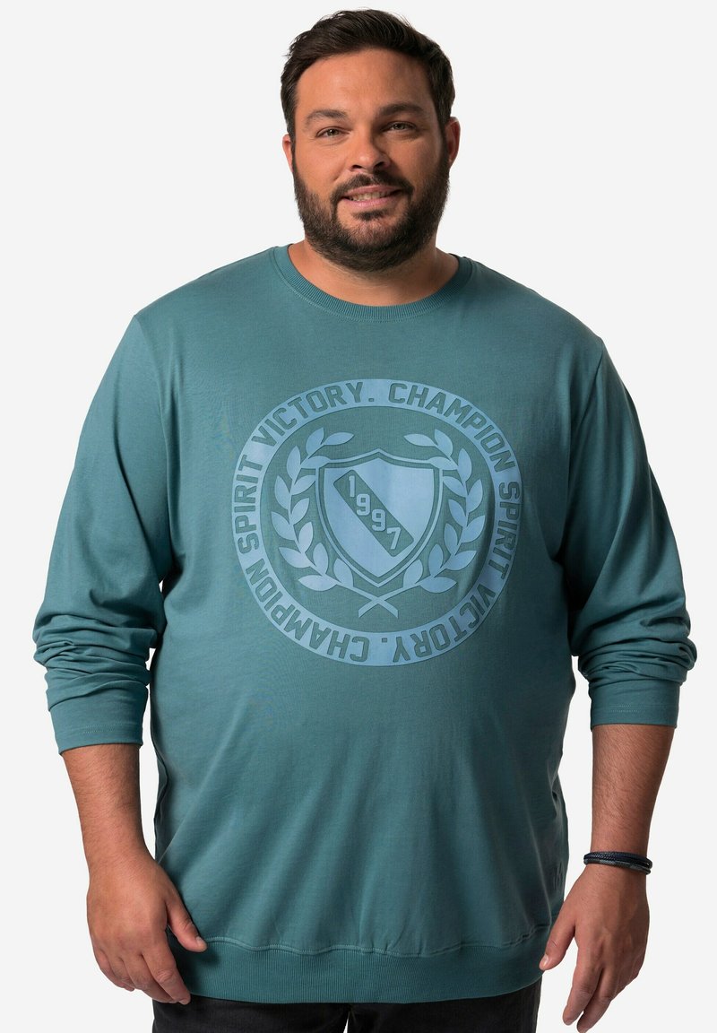 Felpa a maniche lunghe turchese con un design grafico circolare che presenta uno scudo, alloro e testo. Polsini e bordo a coste. Tessuto morbido.
