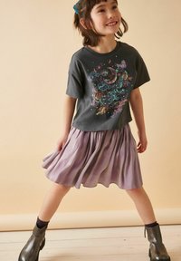 Grå t-shirt med färggrafisk design, ihop med en ljuslila, plisserad kjol. Svarta ankelstövlar fulländar outfiten.