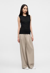 Μαύρη αμάνικη μπλούζα και μπεζ παντελόνι με φαρδιά μπατζάκια, υφή υφάσματος λεία, μινιμαλιστικός σχεδιασμός, συνδυασμένα με λευκά αθλητικά παπούτσια.