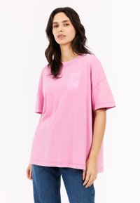 Roze katoenen t-shirt met een losse fit, korte mouwen en een vierkante grafische ontwerp op de borst. Soepele textuur, minimale stikseldetails.