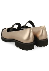 Zapatos planos metálicos dorados con correas elásticas negras, punteras redondeadas y suelas de goma negra texturizada. Superficie lisa y diseño minimalista.