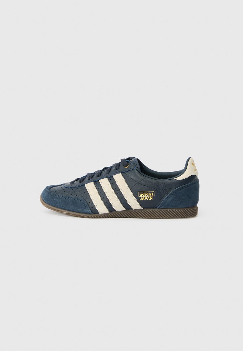 Marineblauwe suede sneaker met crèmekleurige strepen, gestructureerd teenpaneel, gouden "adidas JAPAN" logo en een bruine rubberen zool. Klasseiek laag model.