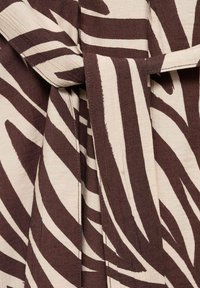 Brun och krämfärgad textil med ett djärvt zebramönster. Materialet verkar mjukt med en något texturerad yta och en knytrem. 
