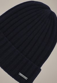 Zrolowana czapka beanie w kolorze granatowym wykonana z dzianiny prążkowanej. Posiada małą metalową metkę marki przyszytą na krawędzi. Miękka w dotyku.