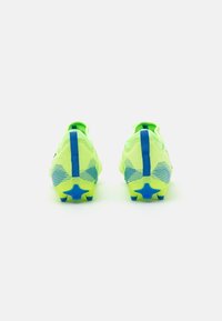 Des chaussures de football néon jaunes avec une surface texturée, des accents bleus et des crampons en forme d'étoile sur la semelle. Présente un renfort au niveau du talon.