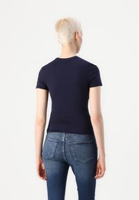 Marineblå kortermet tettsittende t-skjorte, elastisk bomullstoff, rund hals, kombinert med middels høye blå denimjeans med baklommer.
