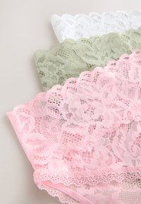 Bandes de tissu en dentelle empilées en blanc, vert olive et rose, avec des motifs floraux et des bords festonnés sur un fond neutre.