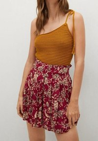 Débardeur en maille couleur moutarde avec bretelle fine, associé à une jupe taille haute bordeaux avec un motif floral et un design plissé.