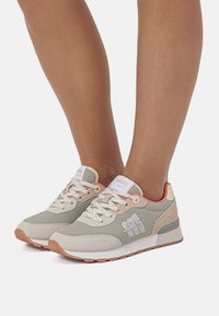 Zapatillas deportivas verdes y beige con parte superior texturizada, puntera redonda, cordones blancos y suela de goma, con un logotipo en el lateral.