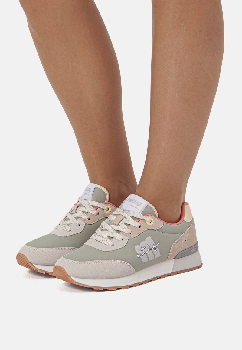 Zapatillas deportivas verdes y beige con parte superior texturizada, puntera redonda, cordones blancos y suela de goma, con un logotipo en el lateral.