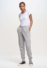 Graue Jogginghosen mit einem elastischen Bund und seitlichen Taschen, kombiniert mit einem enganliegenden weißen Kurzarm-T-Shirt und schwarzen Sneakern.
