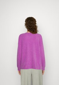 Maglione oversized viola con lavorazione a maglia testurizzata, scollatura rotonda e maniche lunghe, abbinato a pantaloni su misura verde chiaro.