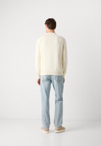 Cream-colored knit sweater with ribbed cuffs and hem, paired with light blue jeans and beige sneakers. Simple design, no patterns or embellishments.