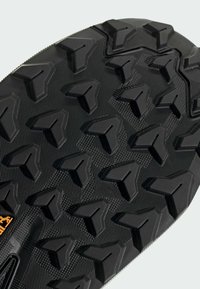 Zwarte rubberen zool met multidirectionele, driehoekige noppen voor grip. Geprofileerd oppervlak met groeven voor flexibiliteit en grip.