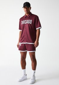 Bordo sportska majica i kratke hlače s bijelim naglascima; majica s natpisom "CHICAGO". Bijele tenisice i crni šešir upotpunjuju odijelo.
