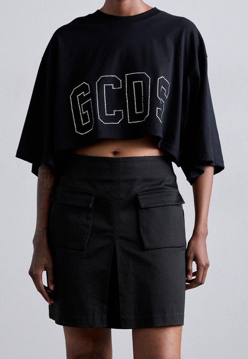 Camiseta negra corta con "GCSD" en pedrería, combinada con una falda negra con bolsillos frontales y una abertura central. Textura de tela suave.