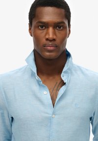 Lichtblauwe button-up shirt van een zachte, gestructureerde stof. Bevat een klassieke kraag en een subtiele logo-detail op de borst.