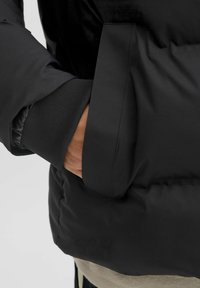 Sort pufferjakke med en glat tekstur, elastiske manchetter og en sidelomme. Materialet ser ud til at være vandafvisende med en mat finish.