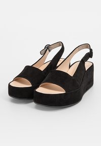 Sandales à talons compensés en daim noir avec un design à bout découvert, une bride de cheville réglable et une doublure intérieure lisse. Présente une semelle plateforme pour plus de hauteur.