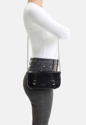 Woman wearing white long-sleeve top and dark jeans with black textured leather crossbody bag featuring silver chain strap and buckle details.
