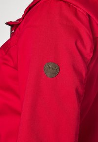 Veste rouge en tissu lisse et texturé. Dispose d'une étiquette en cuir marron avec "ONLY" et "Établi en 1995" sur l'épaule gauche.