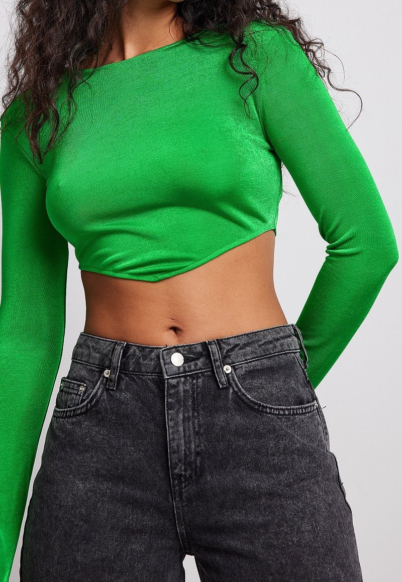 Green long-sleeve cropped top made of smooth fabric paired with high-waisted black denim jeans featuring front pockets and metal button.
