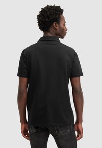 Schwarzes Polohemd mit kurzem Kragen und kurzen Ärmeln, aus smoothen Stoff gefertigt, von hinten gezeigt mit leichtem Glanz.