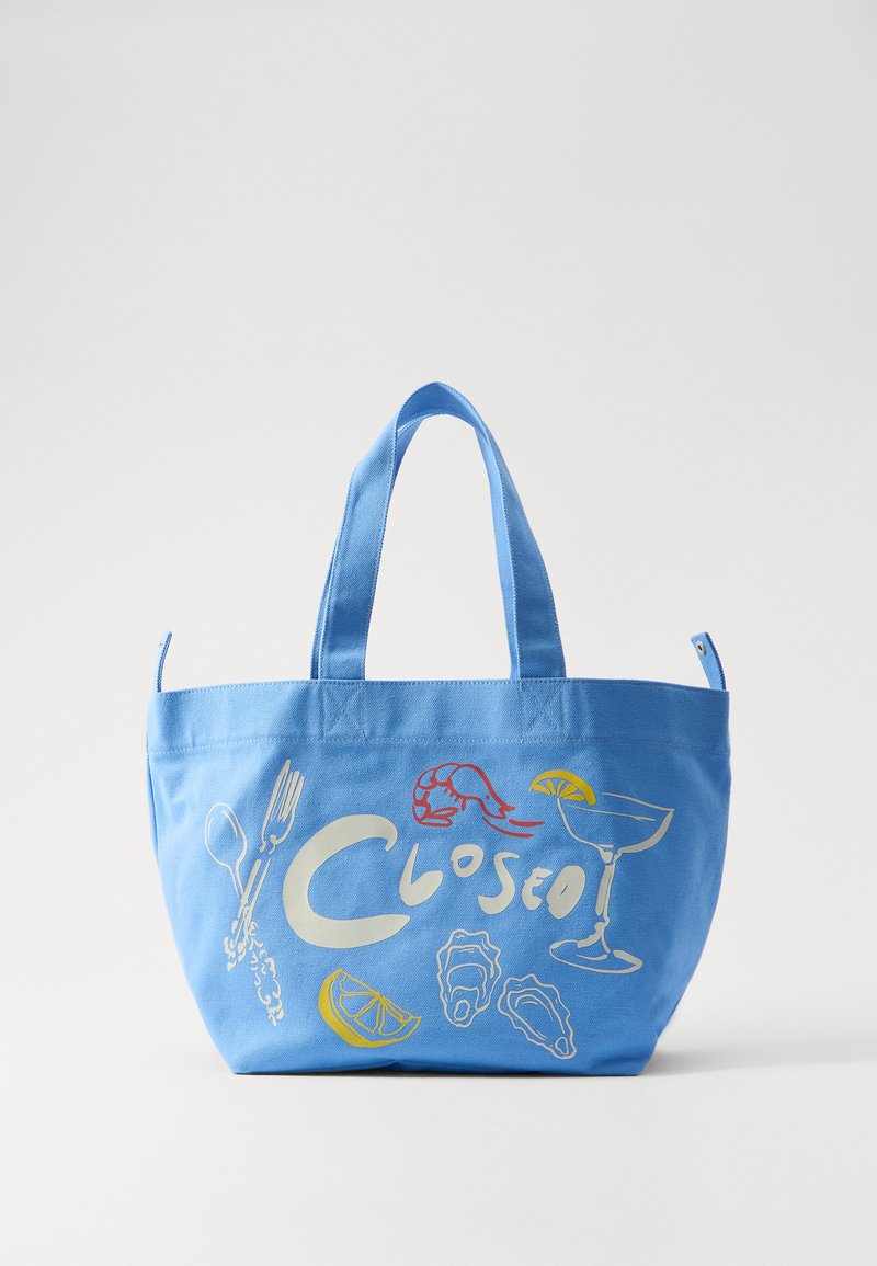 Blue canvas tote bag featuring white and yellow illustrations of food items and the word "Closed." Two sturdy handles for carrying.