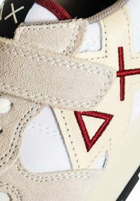 Sneaker bianca con accenti in suede beige, caratterizzata da design triangolari ricamati in rosso e dettagli neri e grigi sul tallone.