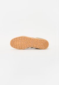 Talpa de sneaker din cauciuc de culoare maro deschis cu modele de prindere circulare; are o margine ondulată și un detaliu cu logo embossat în centru.