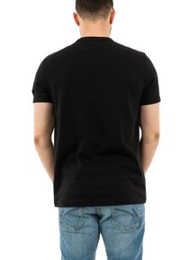Camiseta negra de manga corta con cuello redondo clásico, hecha de una tela suave. Llevada con jeans de color azul claro que presentan costuras decorativas en los bolsillos.