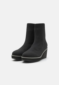 Bottines noires avec un dessus en tricot extensible, bout arrondi et talon en coin. Texture lisse avec une semelle et un liseré en caoutchouc contrastants.