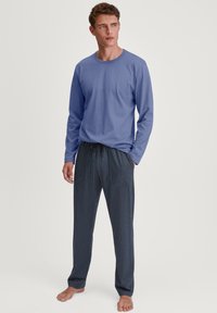 Langsleeve blauwe top gecombineerd met donkere marineblauwe pyjamabroek met een klein wit geometrisch patroon; zacht materiaal, ontspannen pasvorm en een trekkoord in de taille.