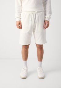 Hvite waffle strikkede shorts med elastisk snor i midjen og lengde over kneet, sammen med hvite sokker og joggesko.
