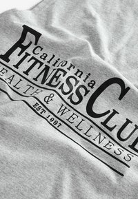 Šedá tkanina má velký černý text s nápisem "California FITNESS CLUB" a menší text "HEALTH & WELLNESS EST 1997" níže.