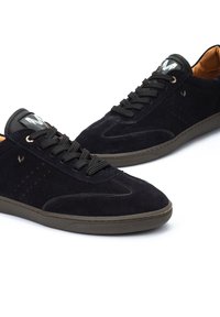 Zapatillas de ante negro con una textura suave, puntera redondeada, detalle de perforaciones mínimas, cordones negros y un interior marrón. Suela de goma.