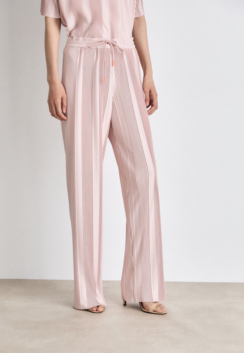 Helle rosa, plissierte weit geschnittene Hose mit einem Kordelzugbund. Der Stoff hat eine glatte Textur und vertikale Streifen für zusätzliche Details.