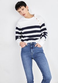 Gestreepte trui in wit en marineblauw met een ronde hals en knoopdetail op de schouder, gecombineerd met hoge taille blauwe jeans.