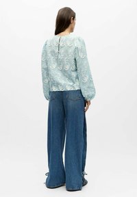 Lichtblauwe geborduurde blouse met lange mouwen; ingewikkeld bloemmotief; gecombineerd met losse, hooggetailleerde blauwe denim broek met gestrikte enkels.