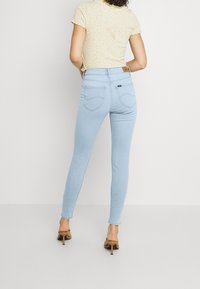 Los jeans skinny de color azul claro tienen una cintura alta, costuras en contraste y dos bolsillos traseros. Se combinan con una blusa corta de manga con estampado floral.
