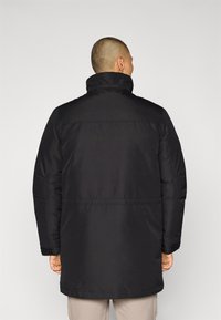 Chaqueta acolchada negra con cuello alto, que presenta una textura lisa y un corte recto. Hay una costura horizontal en la parte posterior.